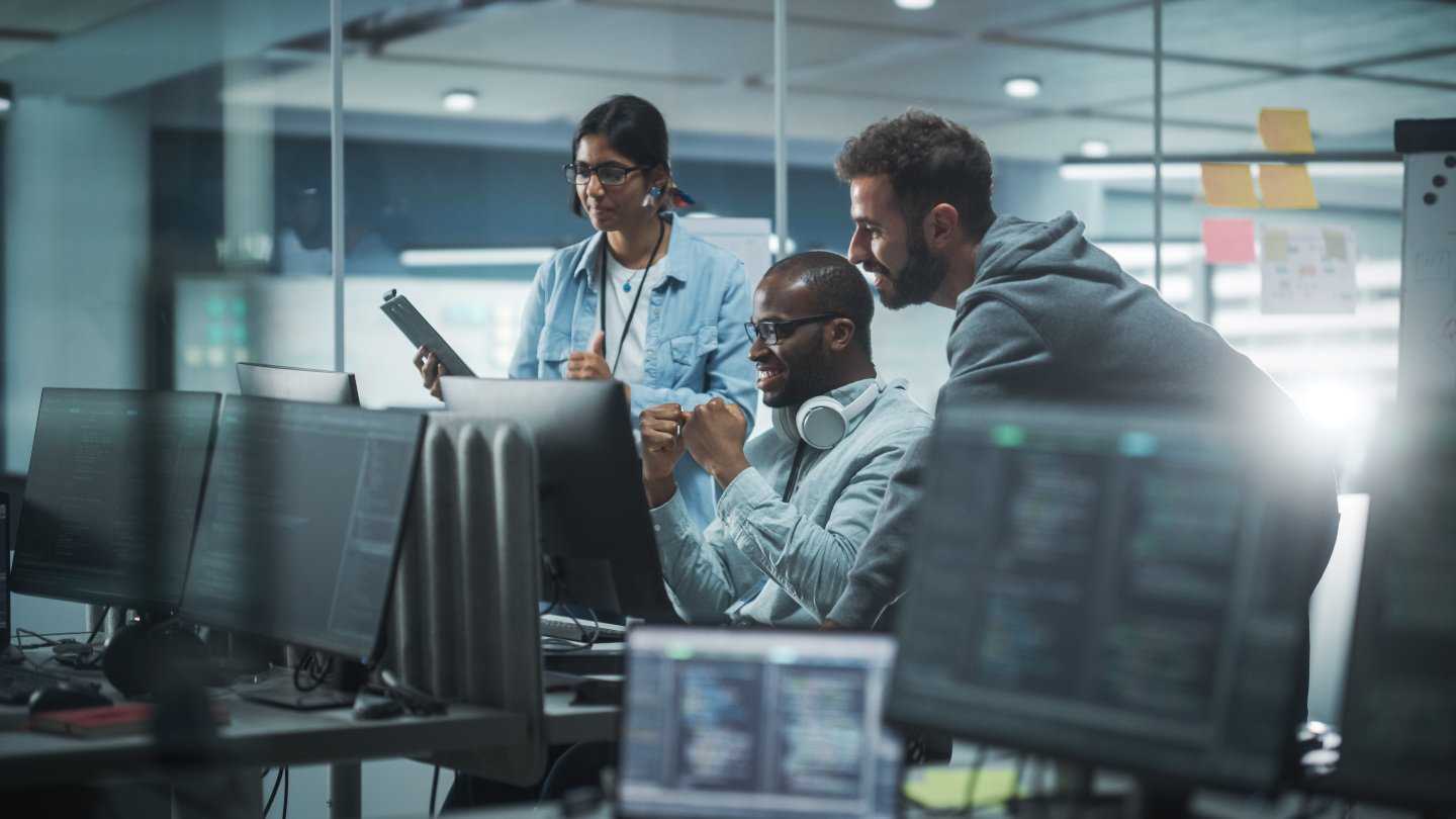 Three people looking at one computer monitor. They are happy with what they see..